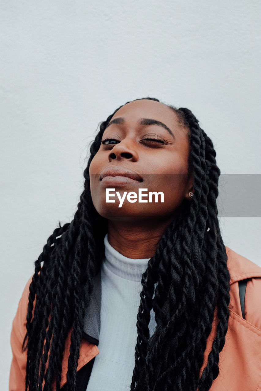 Portrait of young woman winking against wall