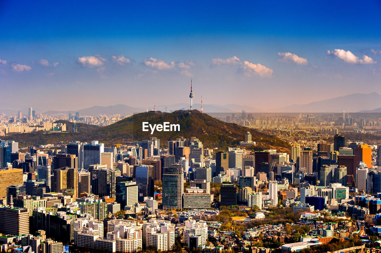 Distant view of n seoul tower on namsan mountain amidst cityscape against sky