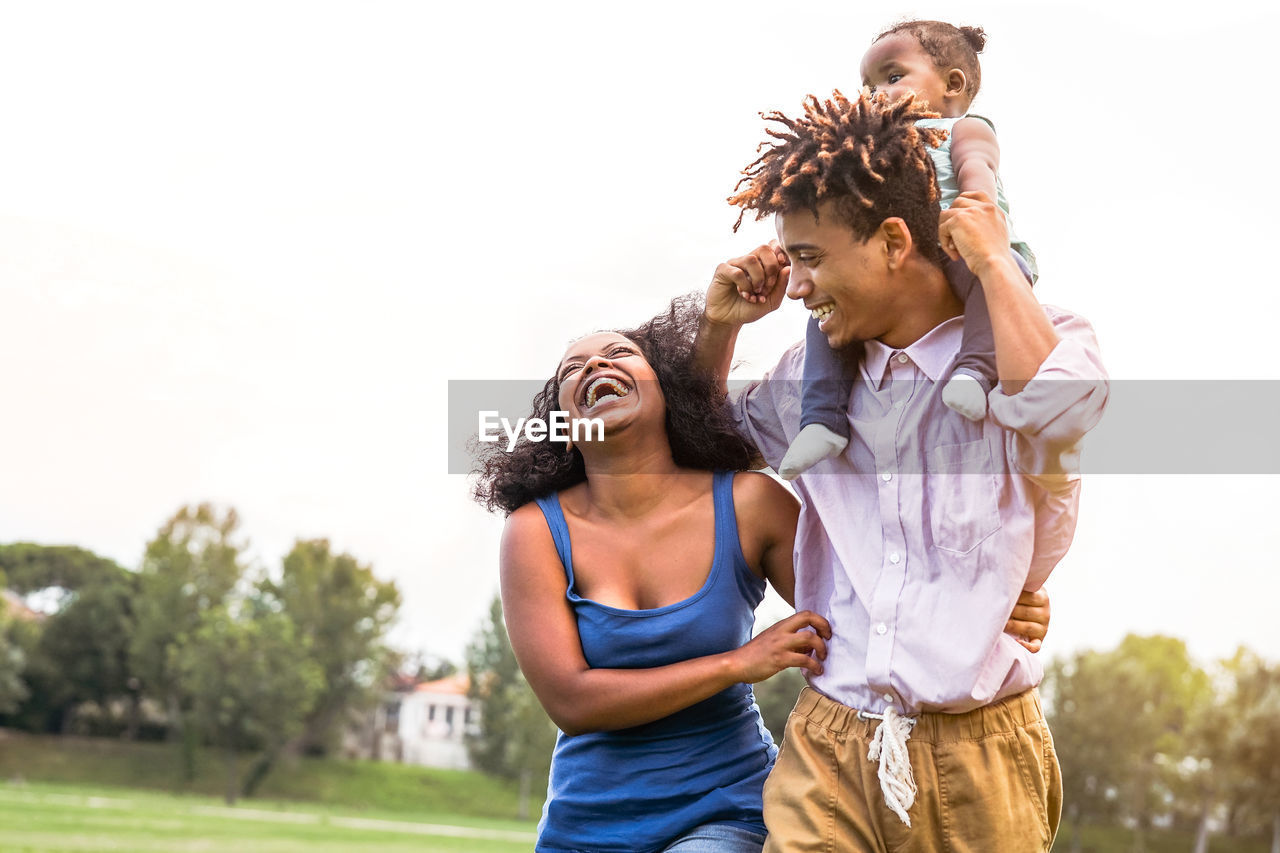 Cheerful mother with arm around father carrying daughter on shoulders