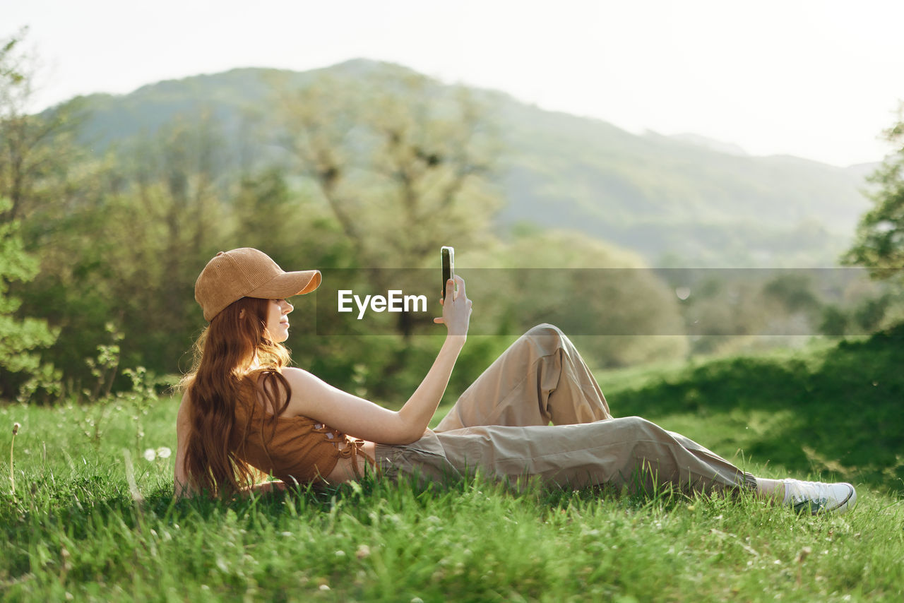 rear view of woman sitting on grassy field against mountain