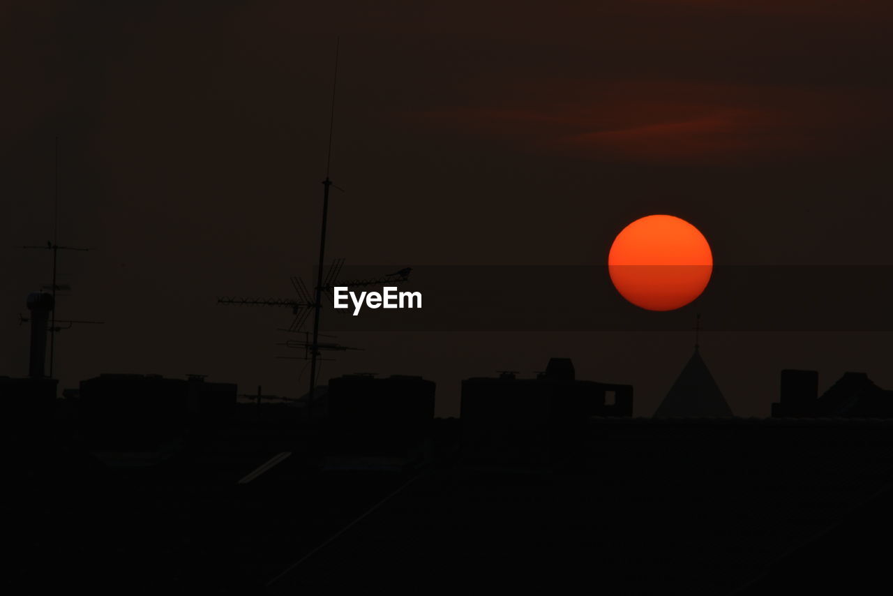 Scenic view of orange sun above silhouette buildings during sunset