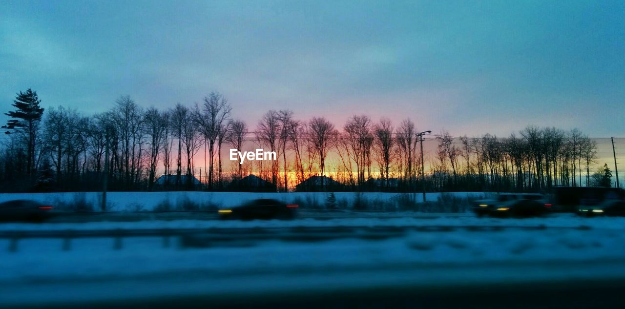 Blurred motion of cars on snow covered street by trees during sunset