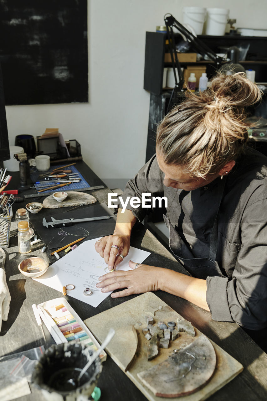 Craftswoman sketching ring design on paper at workbench