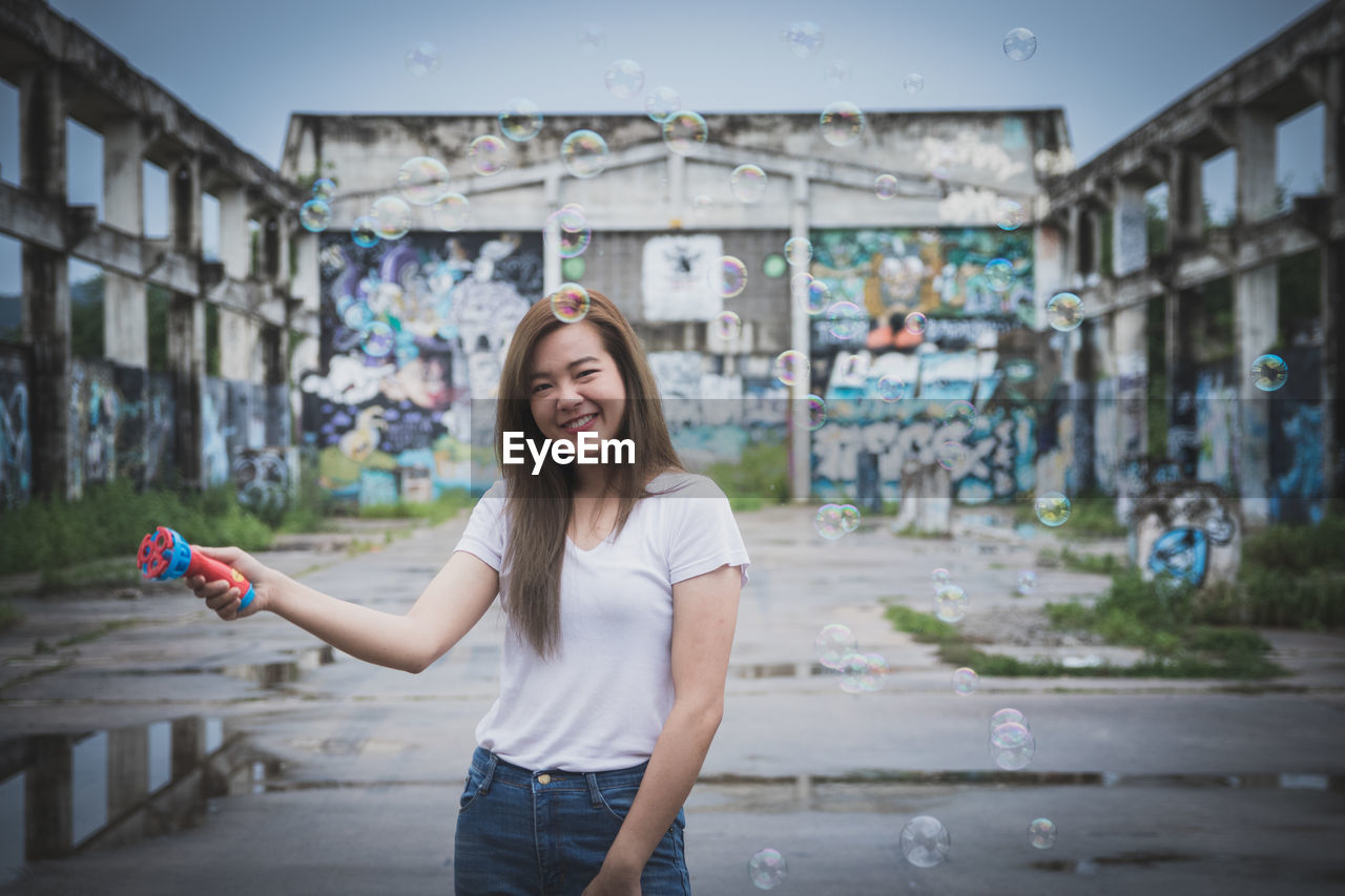 Portrait of smiling young woman blowing bubbles in city