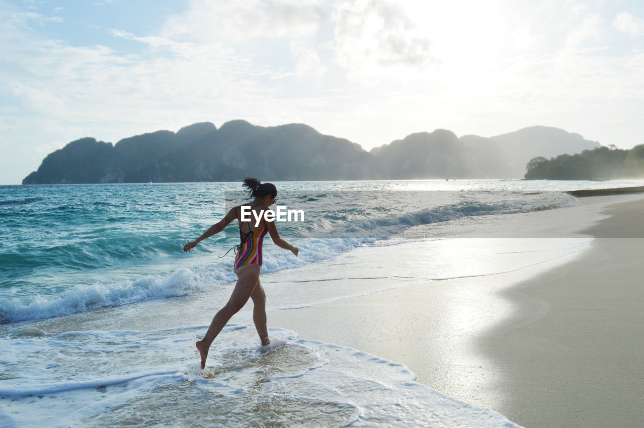 Asian woman in swimsuit running on the shore of koh phi phi island in thailand