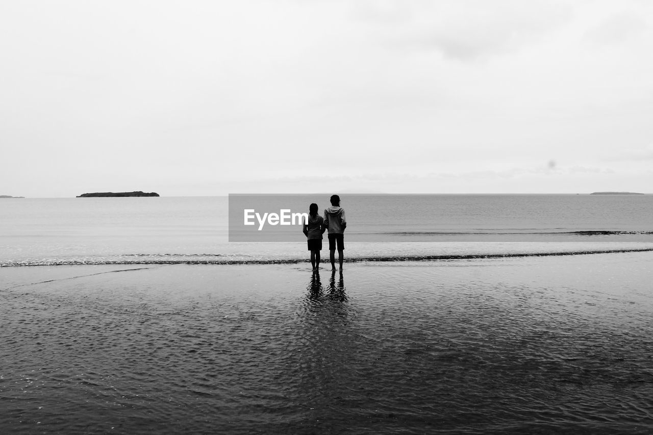 Rear view of friends standing at beach