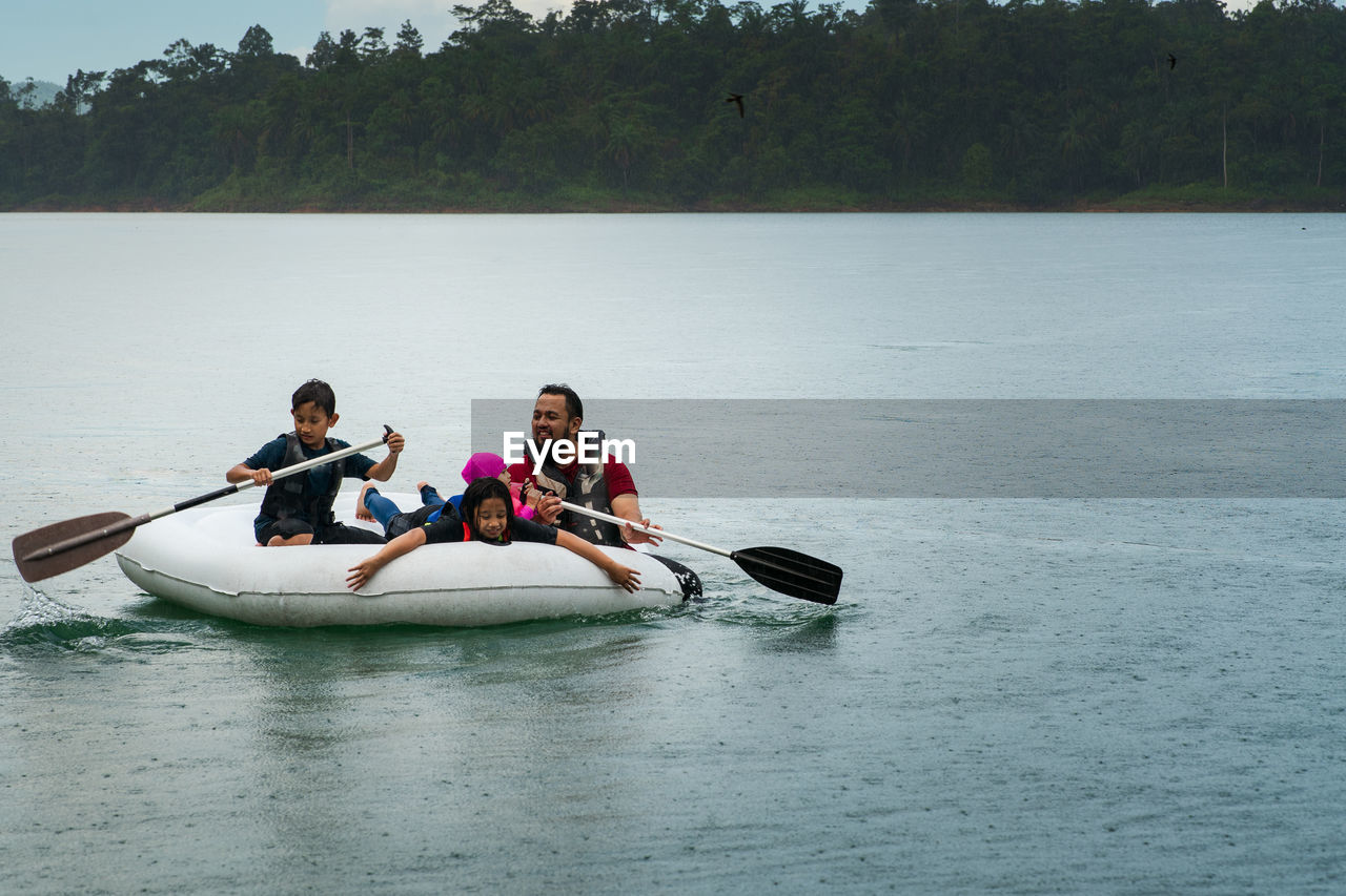 Family wearing life jackets paddling on an inflatable boat in kenyir lake, malaysia.