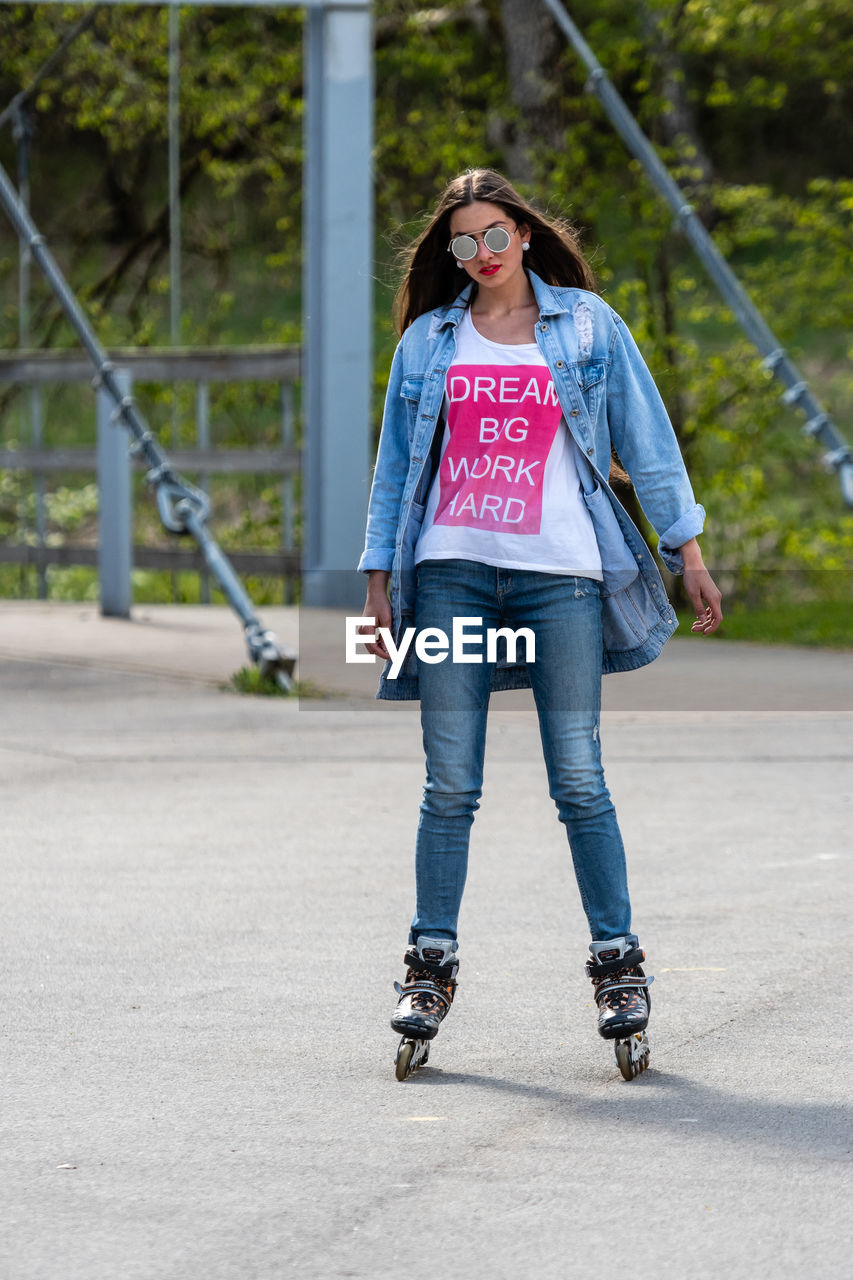 FULL LENGTH PORTRAIT OF YOUNG WOMAN WEARING SUNGLASSES STANDING ON WALKWAY