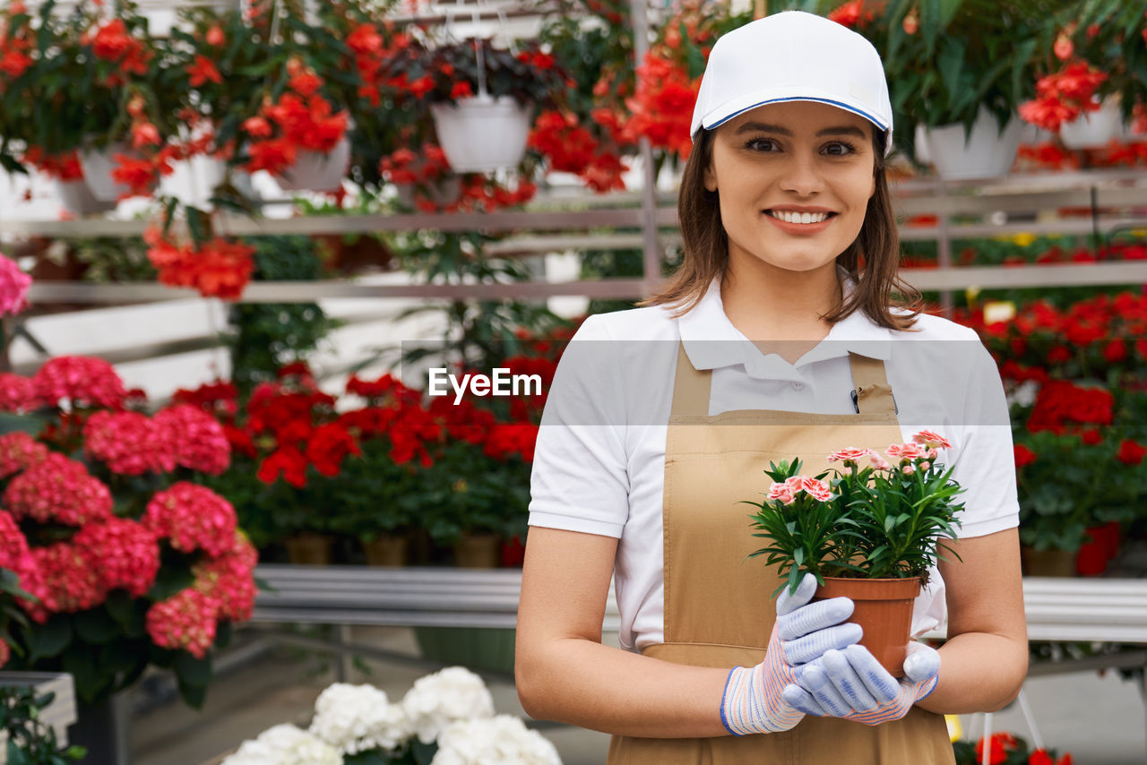 Portrait of young smiling florist holding flowering plants