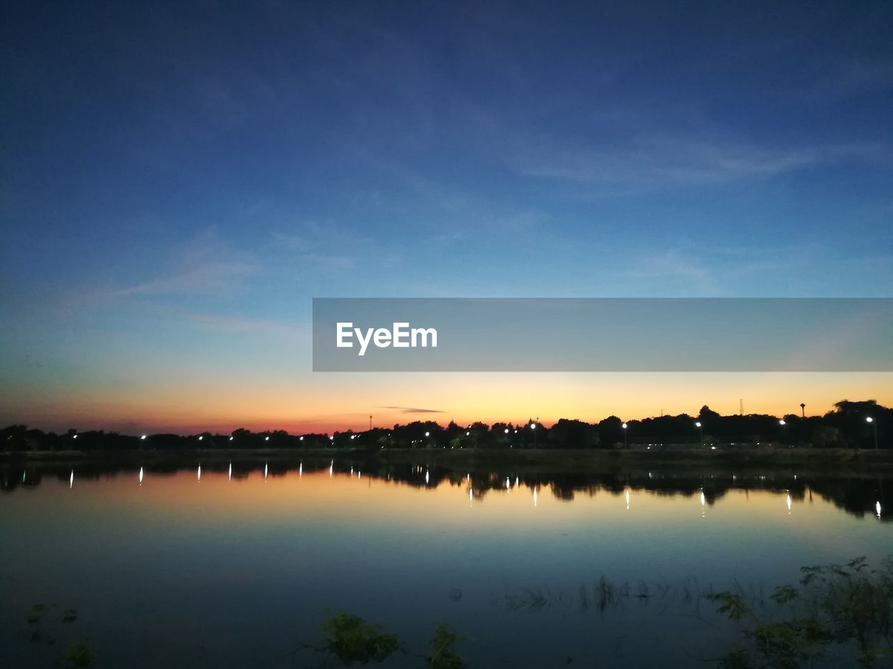 REFLECTION OF SILHOUETTE TREES ON WATER AGAINST SKY