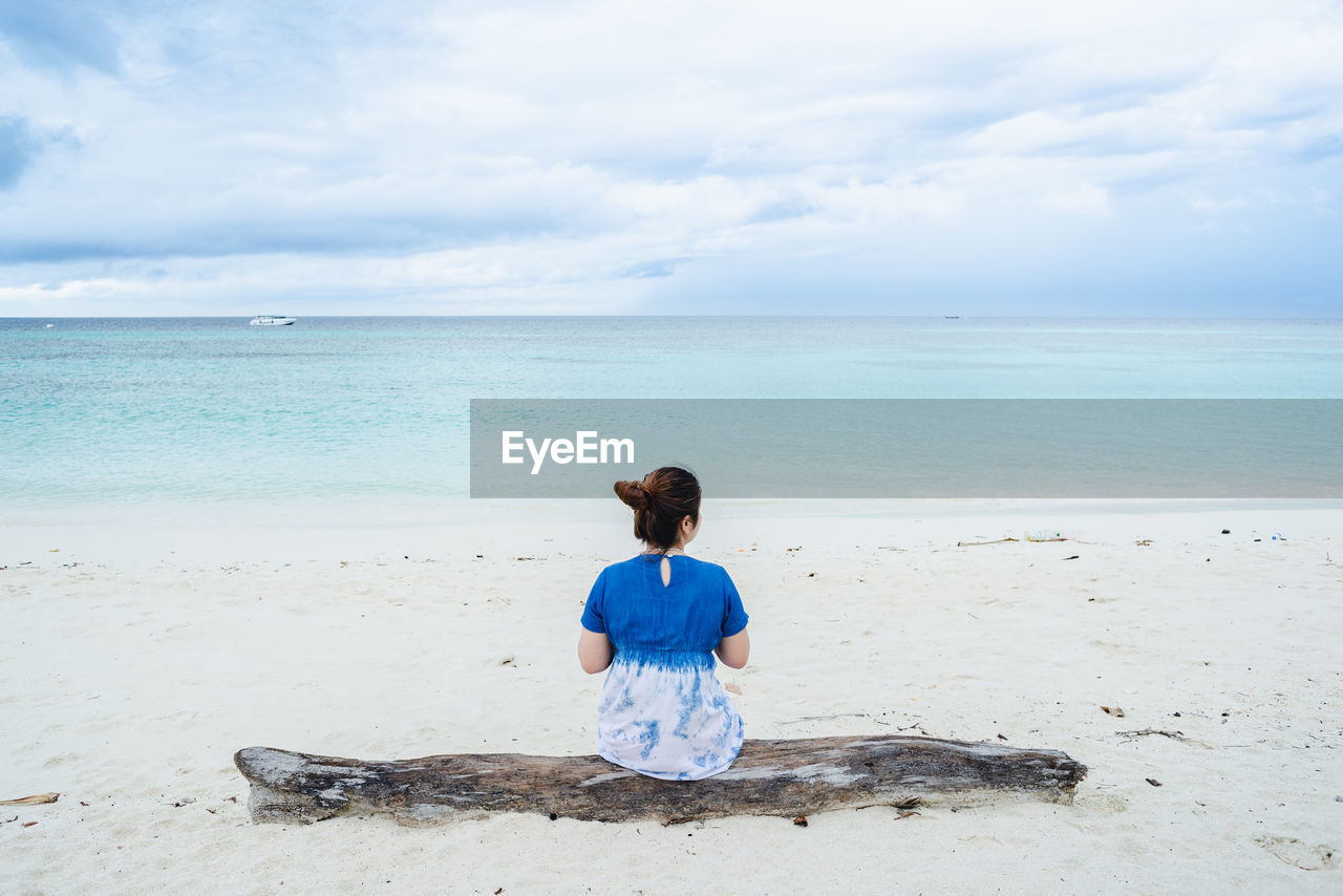 One lady sitting on log and looking away to the beach