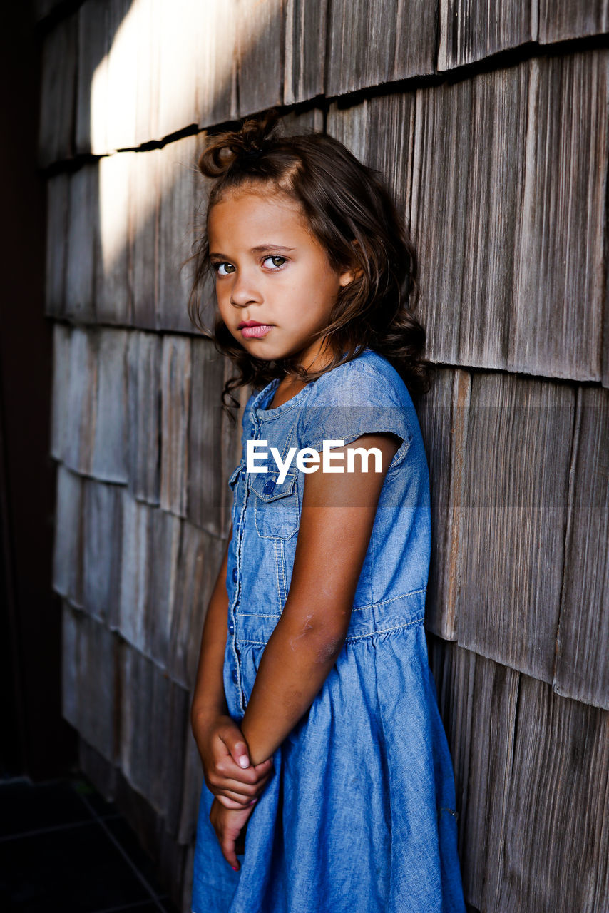 Portrait of girl standing against wooden wall