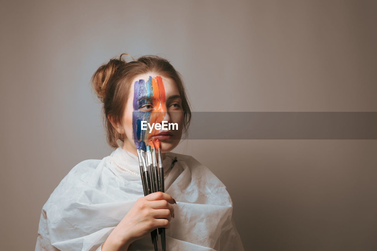 Woman painting face against gray background