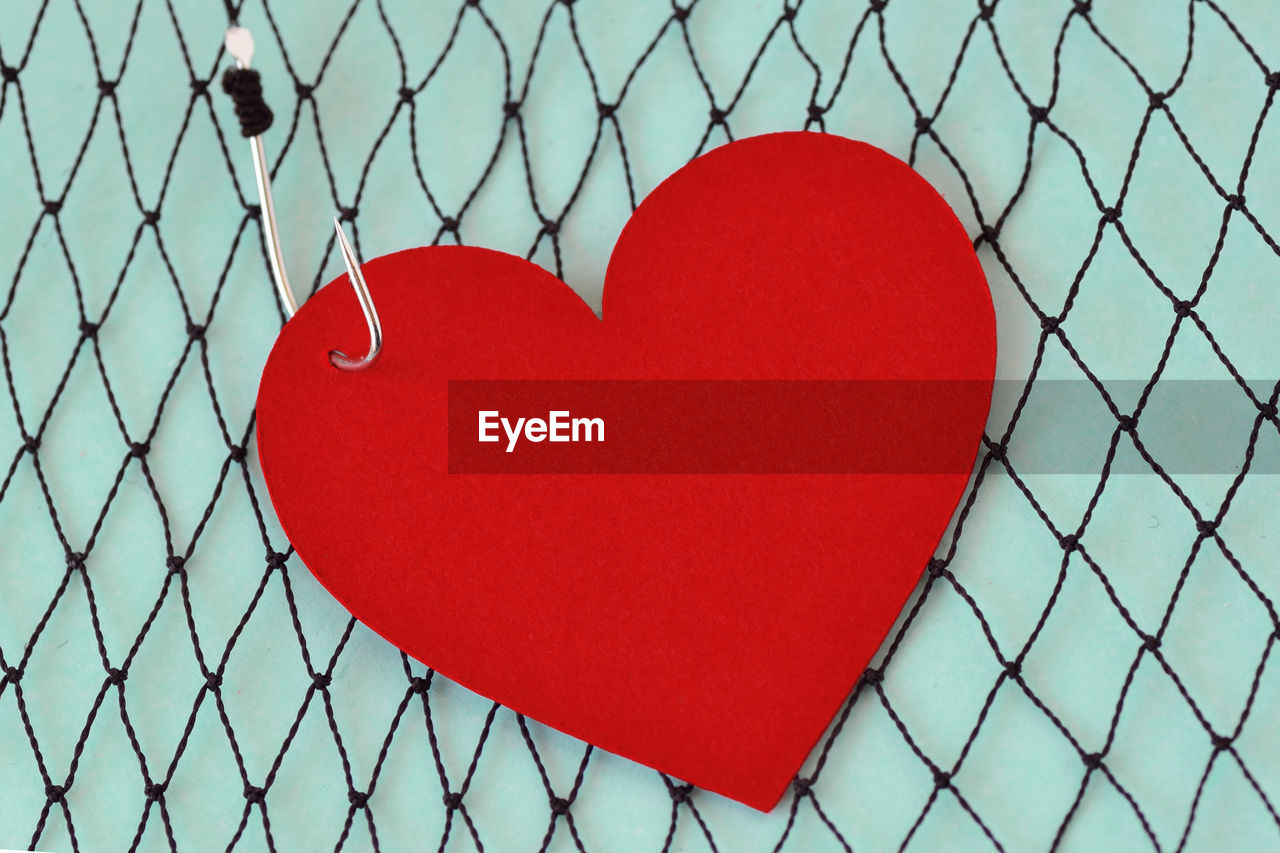 CLOSE-UP OF RED HEART SHAPE ON FENCE AGAINST CHAINLINK WALL