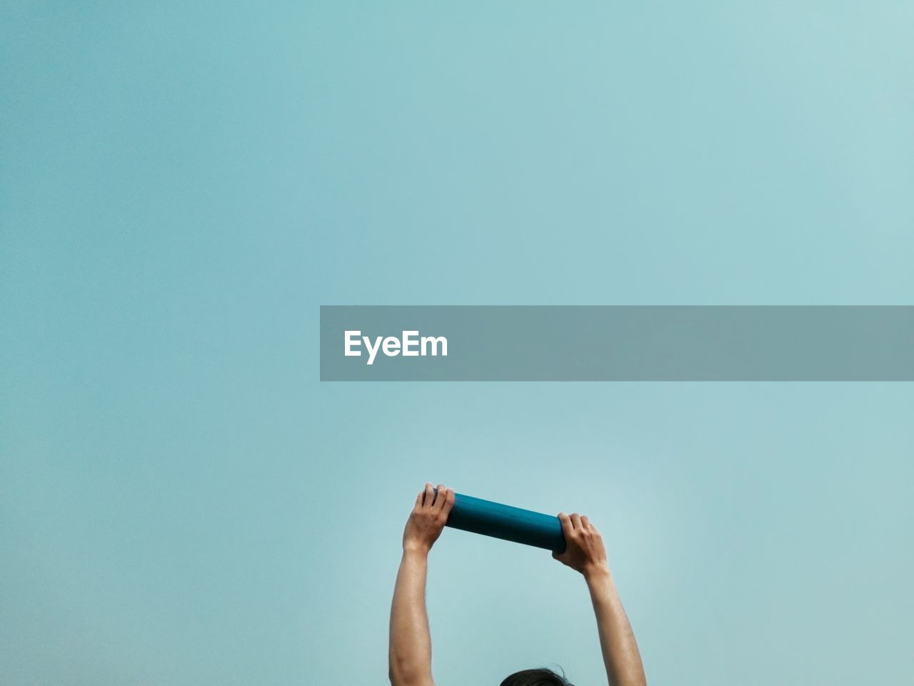 Low angle view of person hand raising loudspeaker against clear blue sky