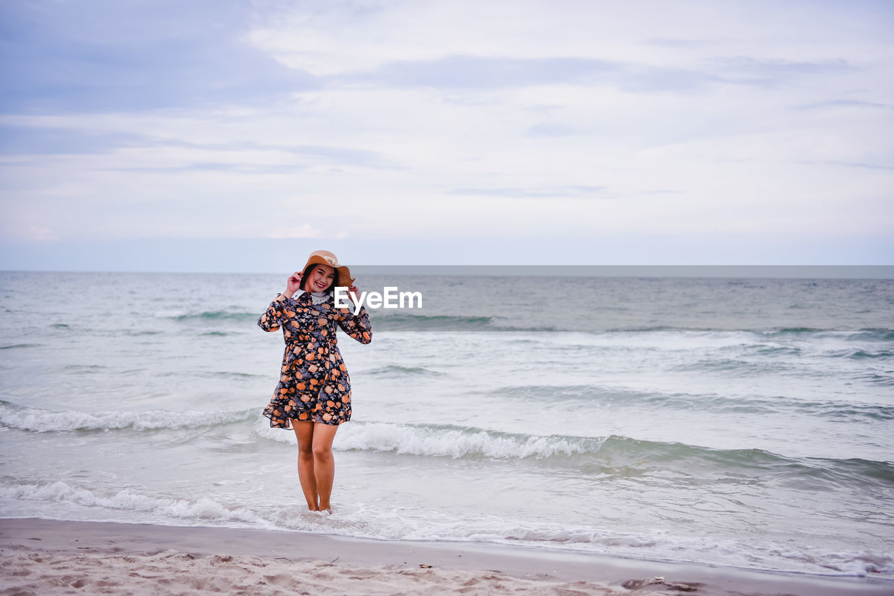 Smiling woman wearing dress standing at beach against sky