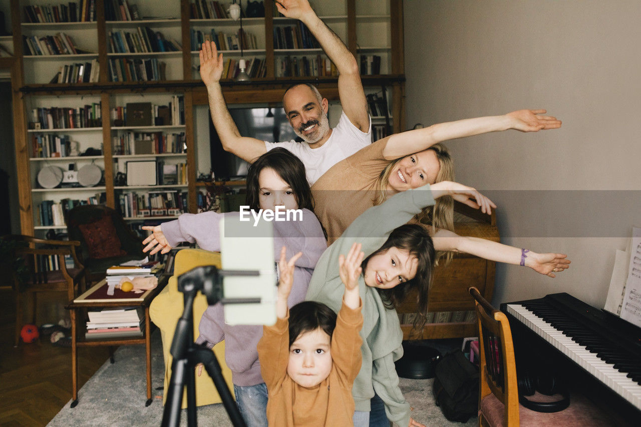 Happy family filming dance with hands raised on smart phone at home