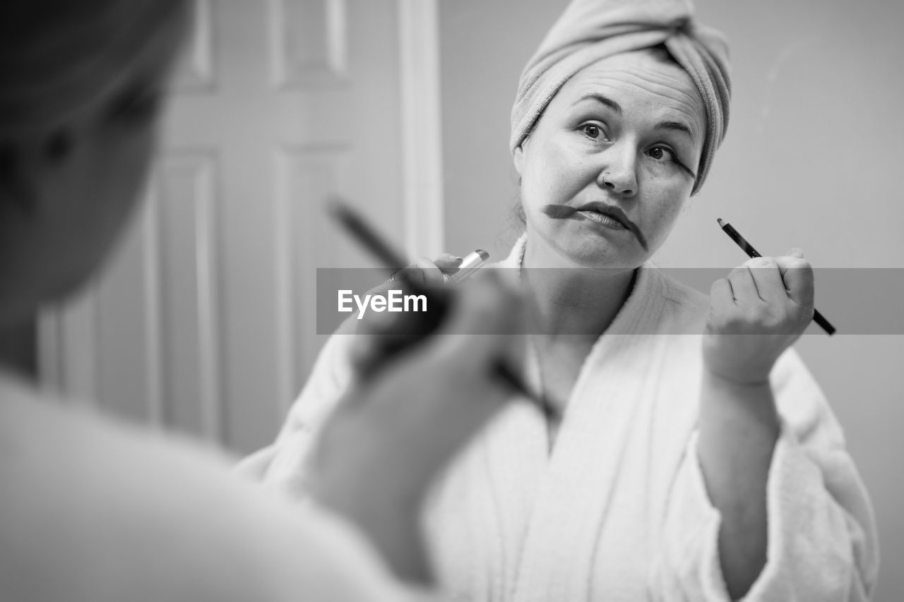 Mature woman applying make-up reflecting on mirror at home