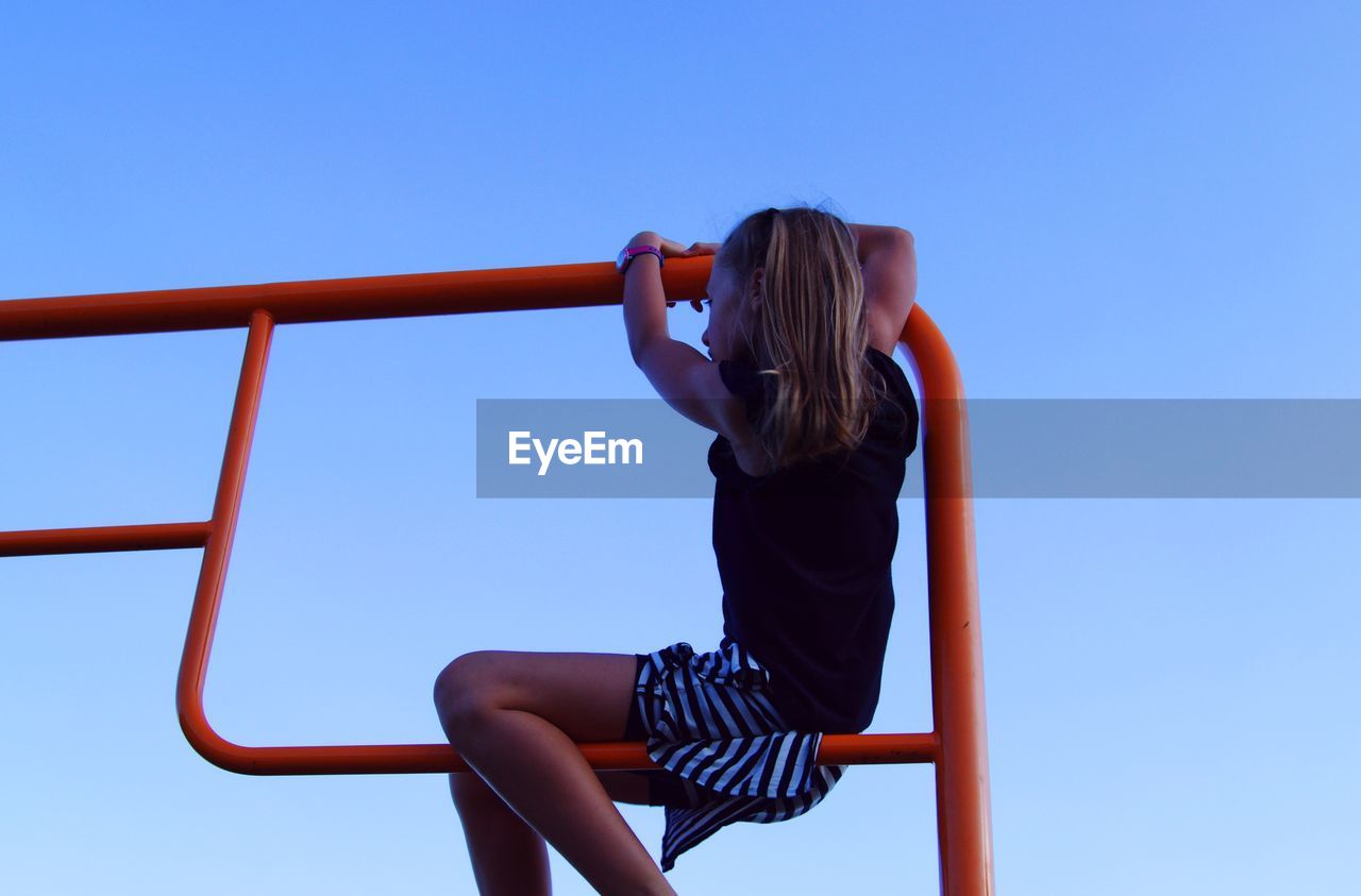 Low angle view of girl playing on railing against clear blue sky