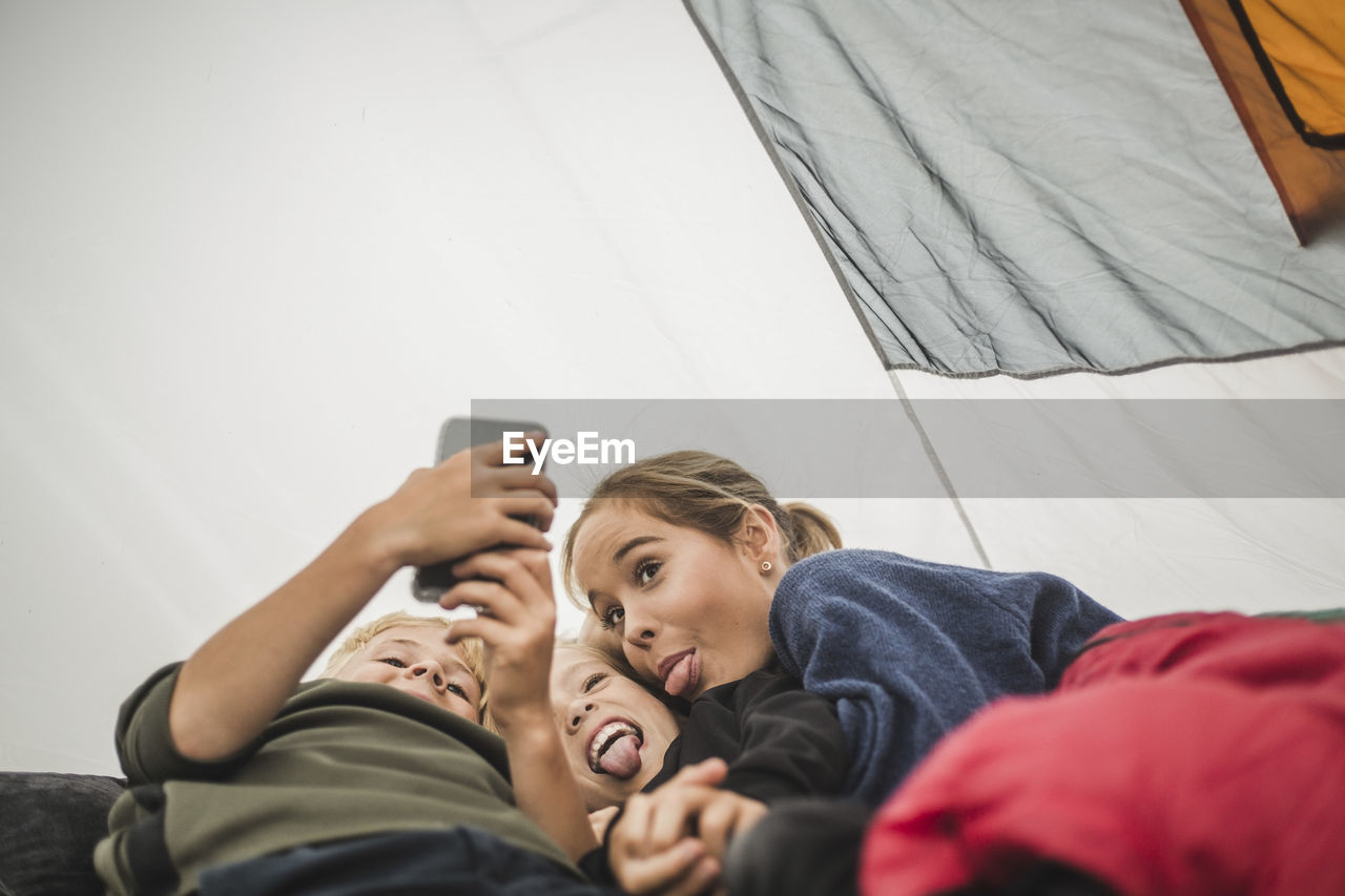 Siblings making face while taking selfie in tent