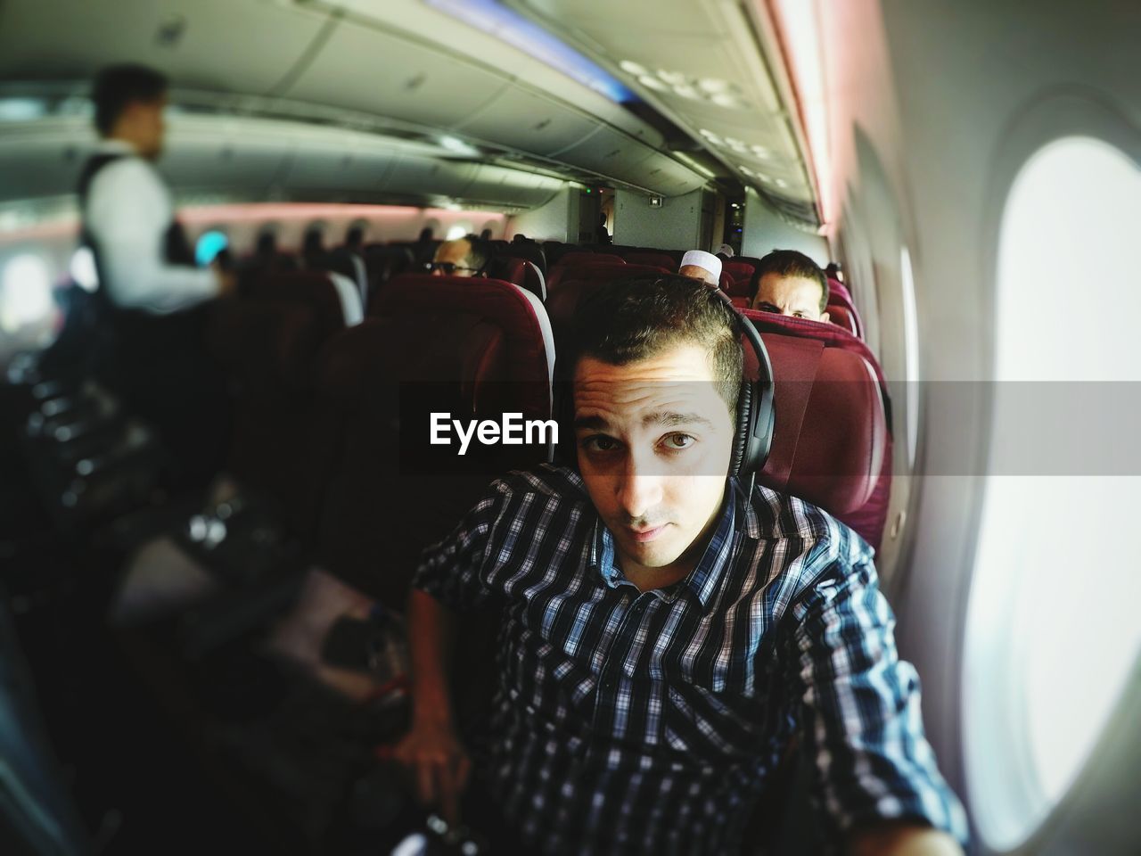 Portrait of man wearing headphones traveling in airplane on sunny day