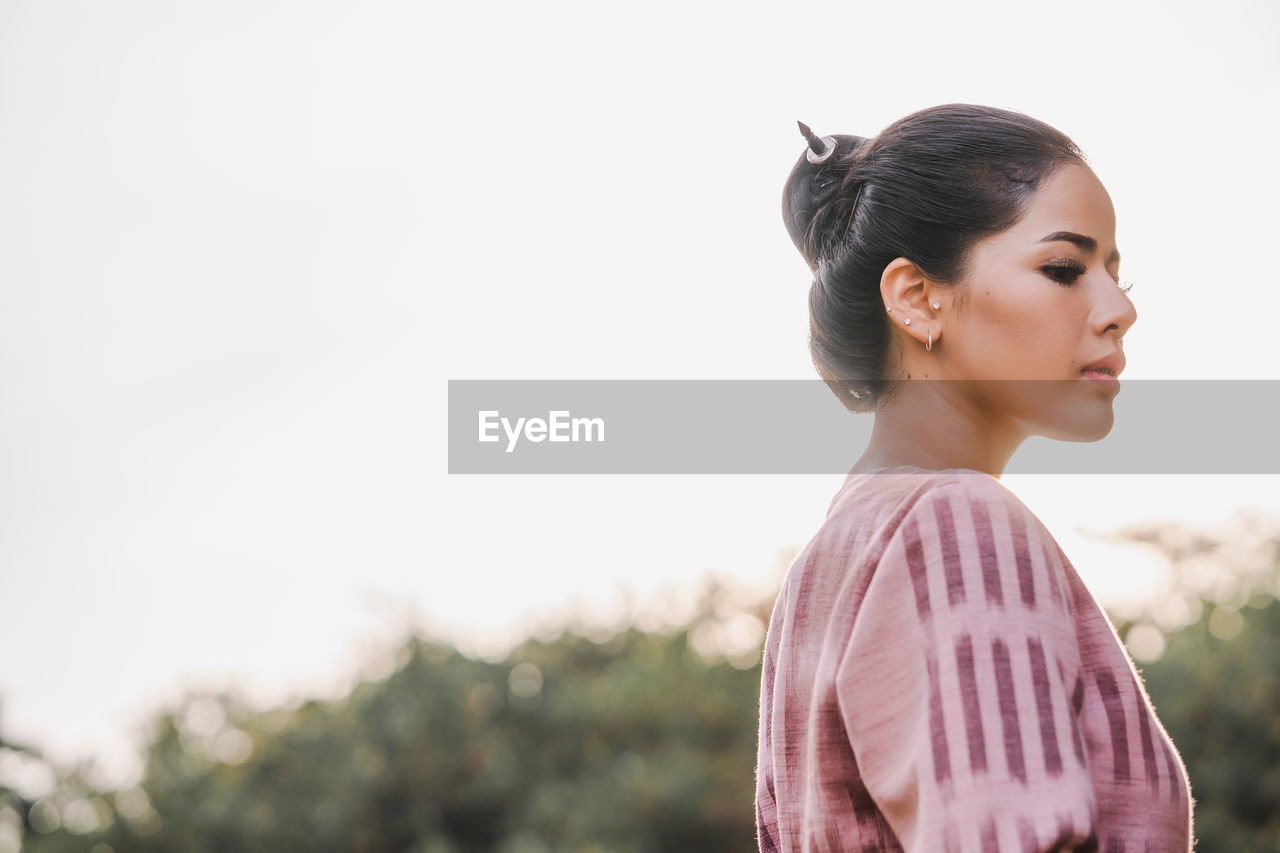 Side view of thoughtful young woman standing against clear sky