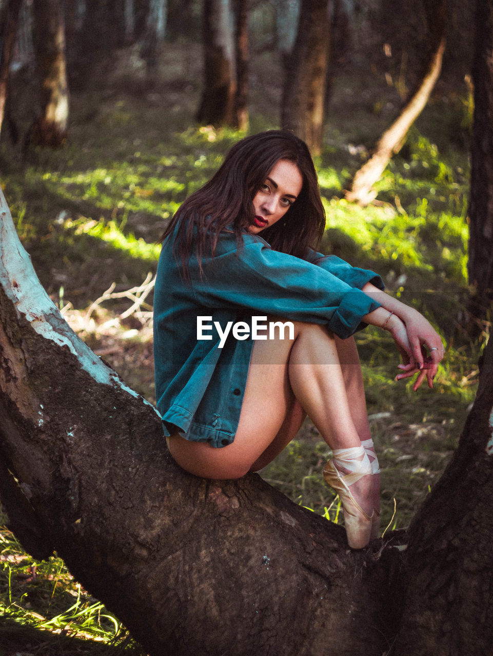 Young dancer sitting on tree trunk in forest