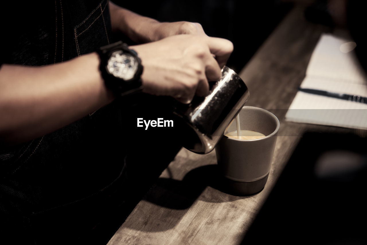 Midsection of man pouring milk in coffee cup