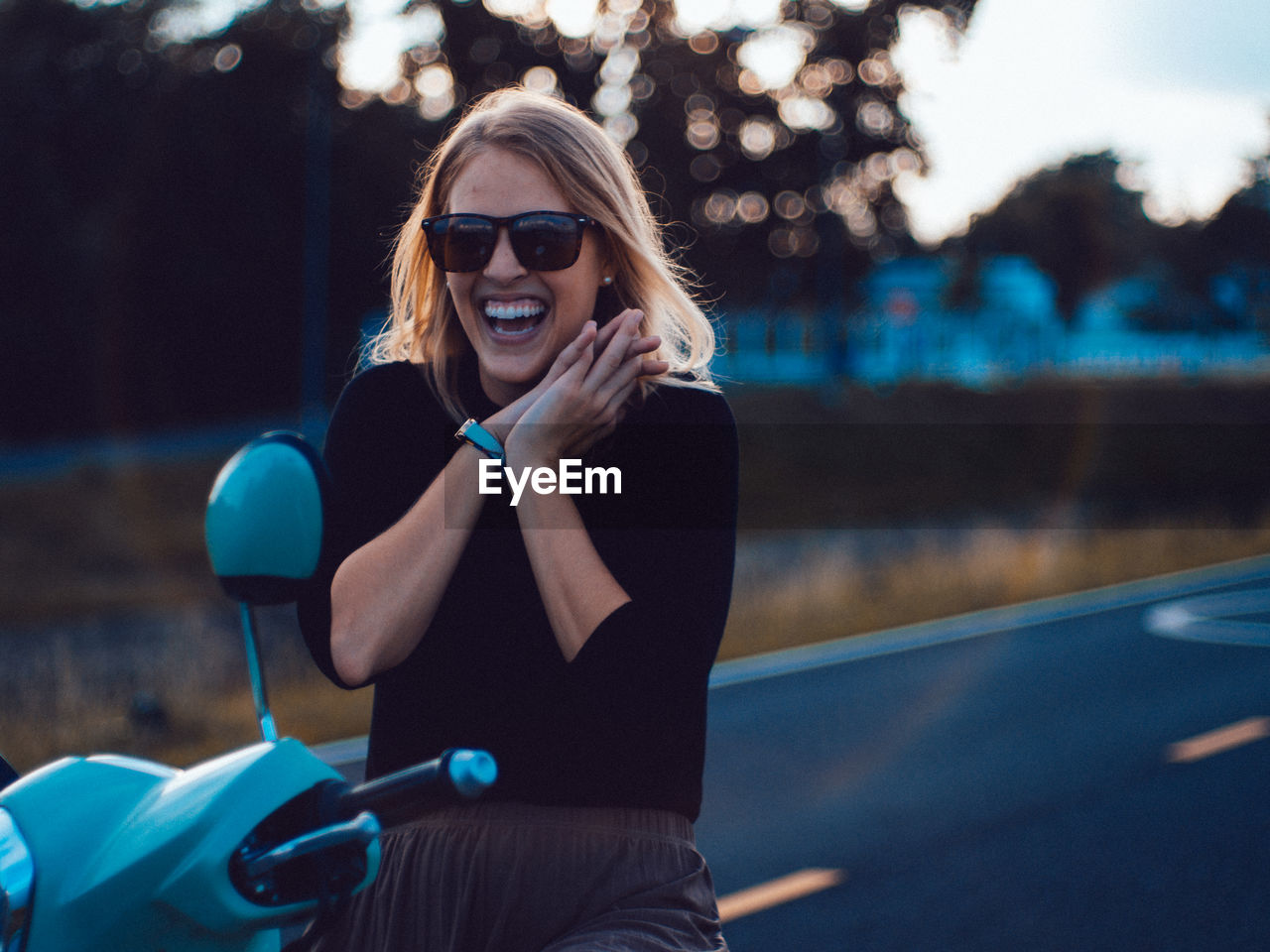 Portrait of cheerful young woman wearing sunglasses sitting on motor scooter