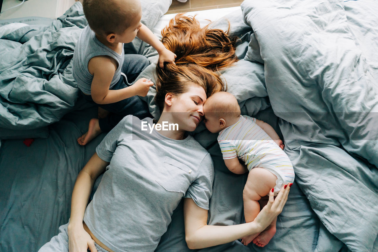 Mommy with two small children lies on the bed and enjoys relationships and motherhood.