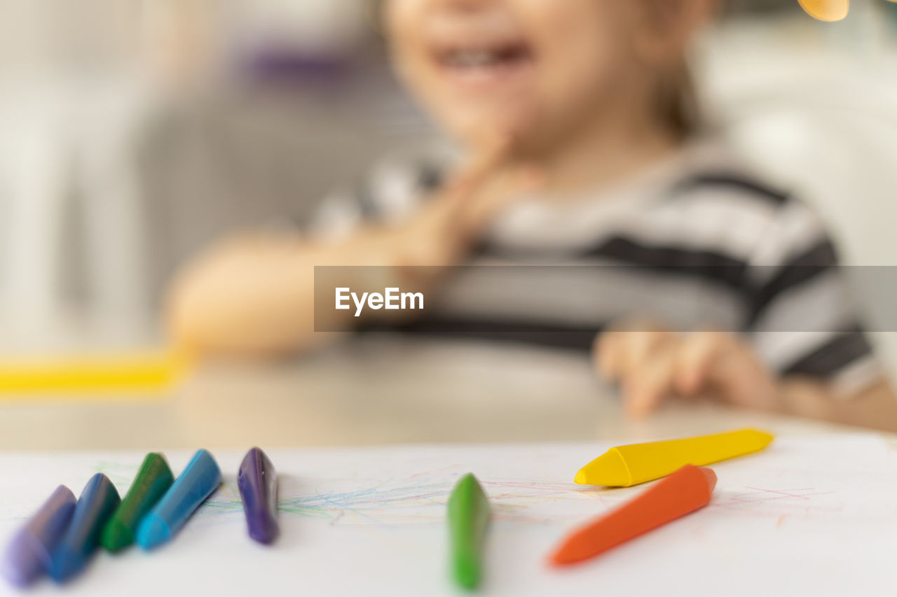 Selective focus on colorful crayons. smiling caucasian baby girl sitting at the table at home