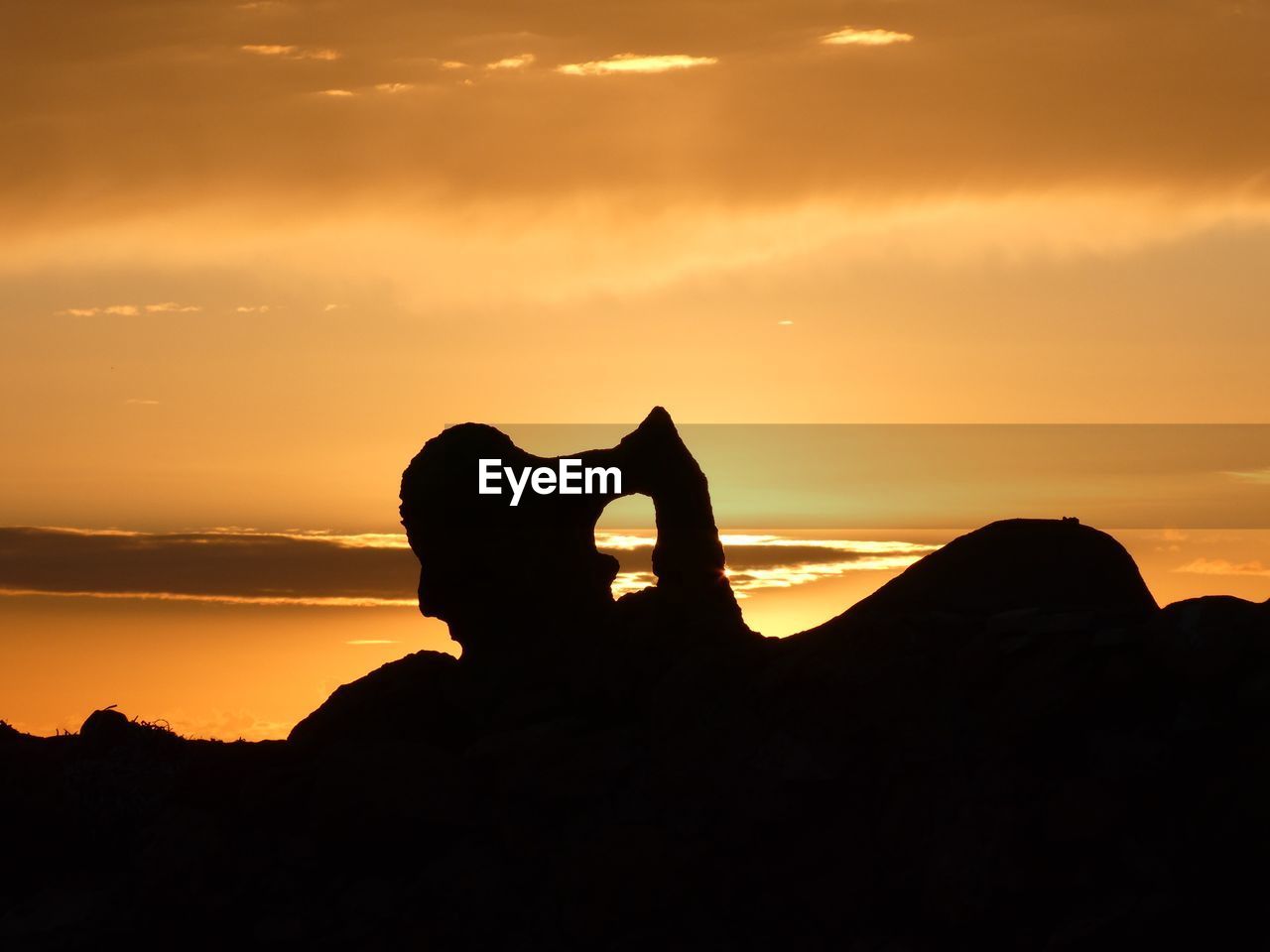 SILHOUETTE MAN ON ROCK AGAINST ORANGE SKY