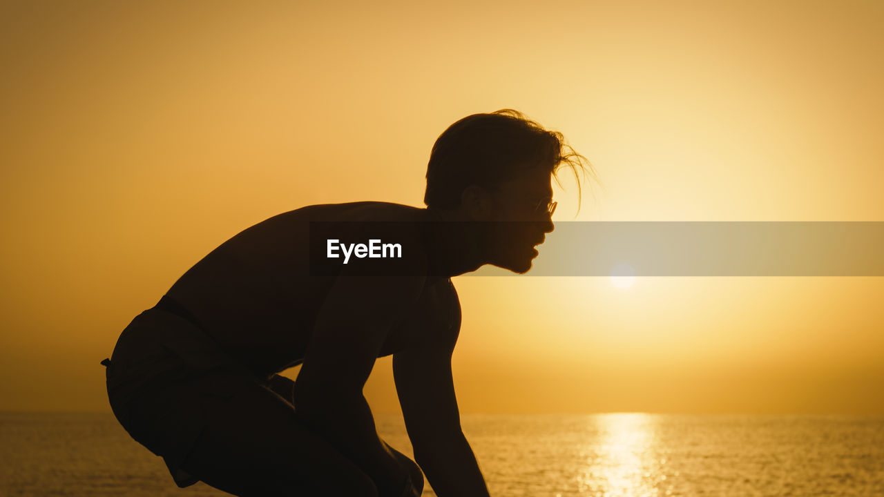 Silhouette of a boy playing american football at dawn on the beach