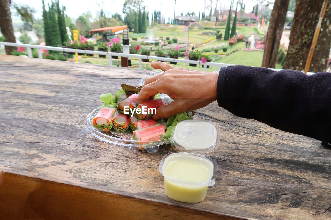 MIDSECTION OF PERSON HOLDING ICE CREAM ON TABLE AT CAFE