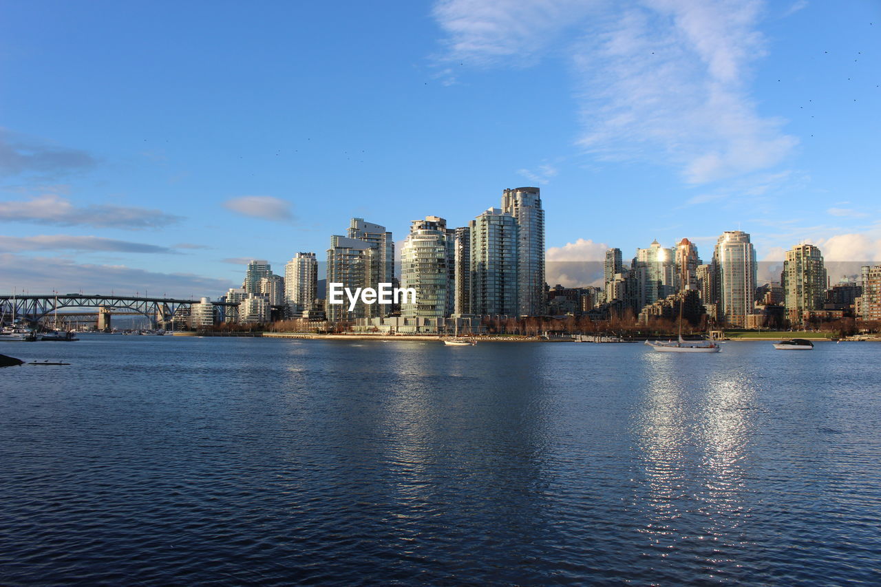 Lake by cityscape against sky 