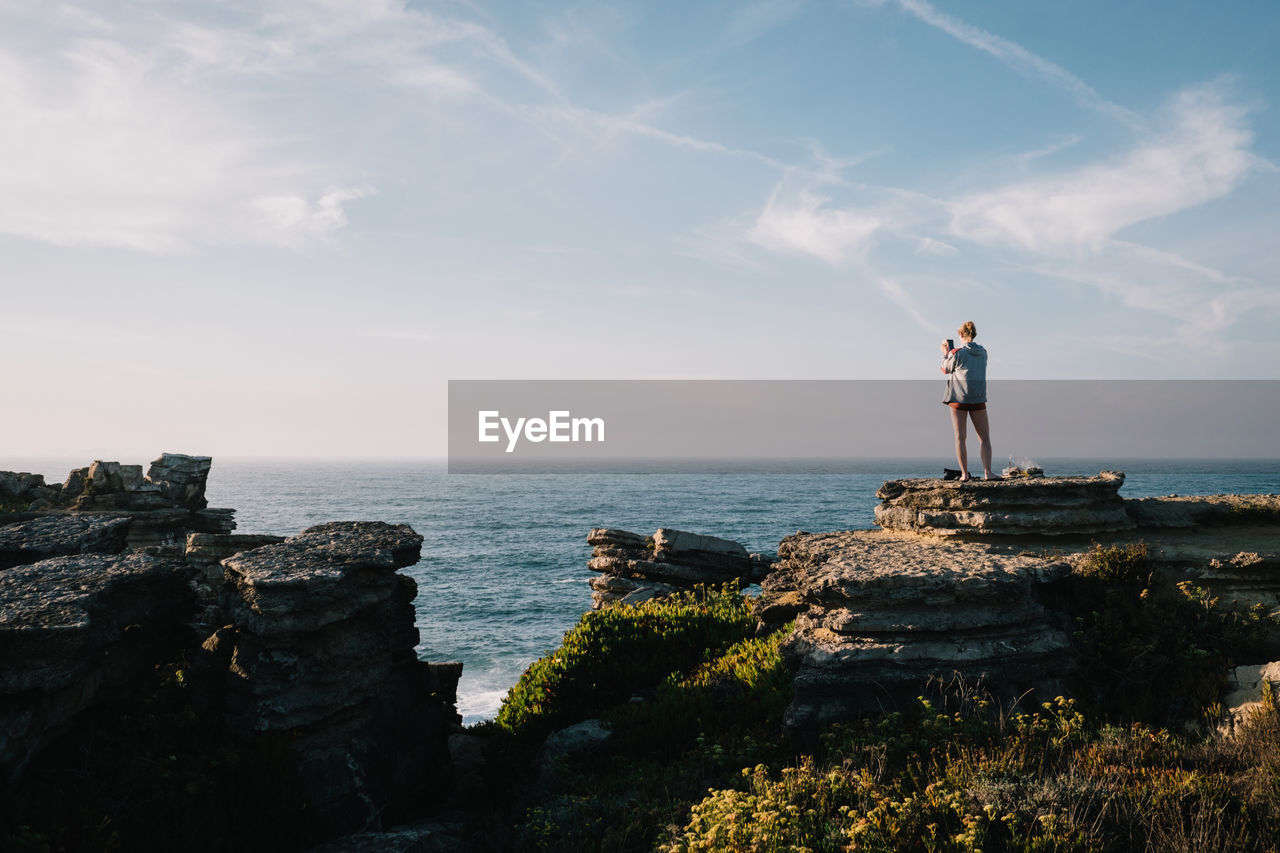 Woman standing on rock by sea against sky