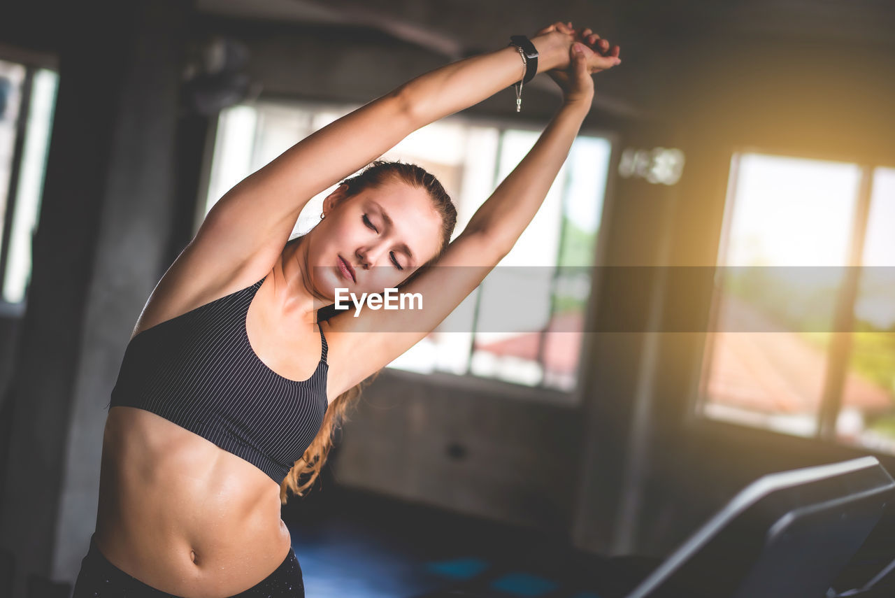 Young woman with arms raised exercising in gym