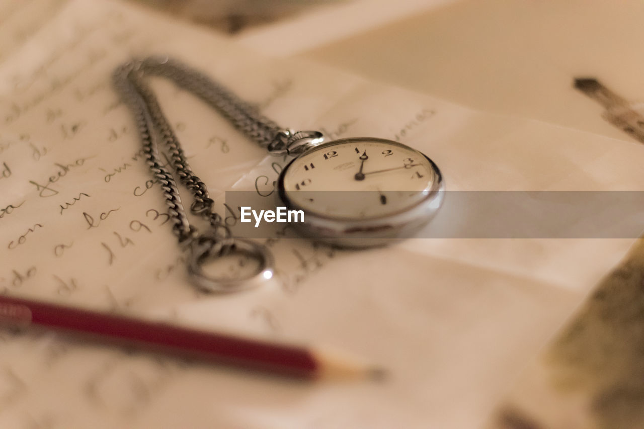 High angle view of pocket watch and pencil on letter