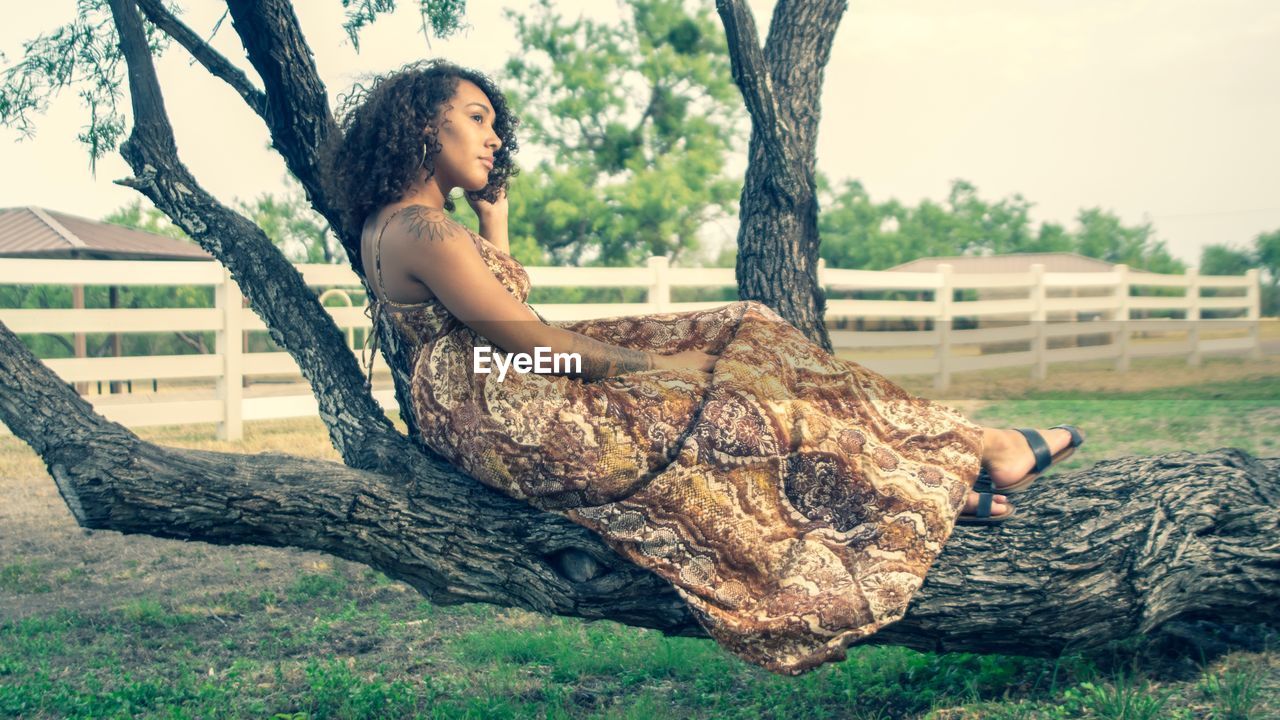 WOMAN SITTING ON TREE TRUNK