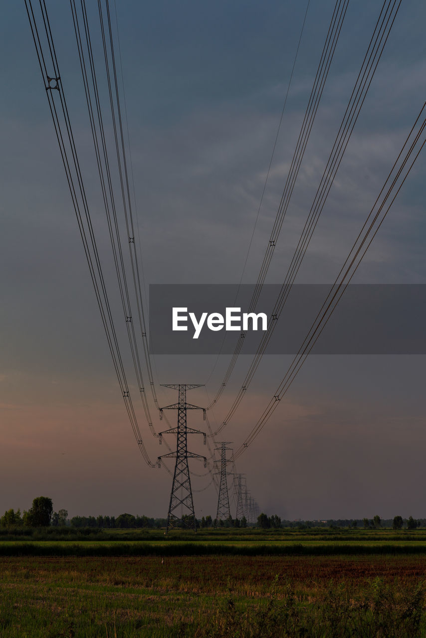 High voltage power lines in a field against a sunset