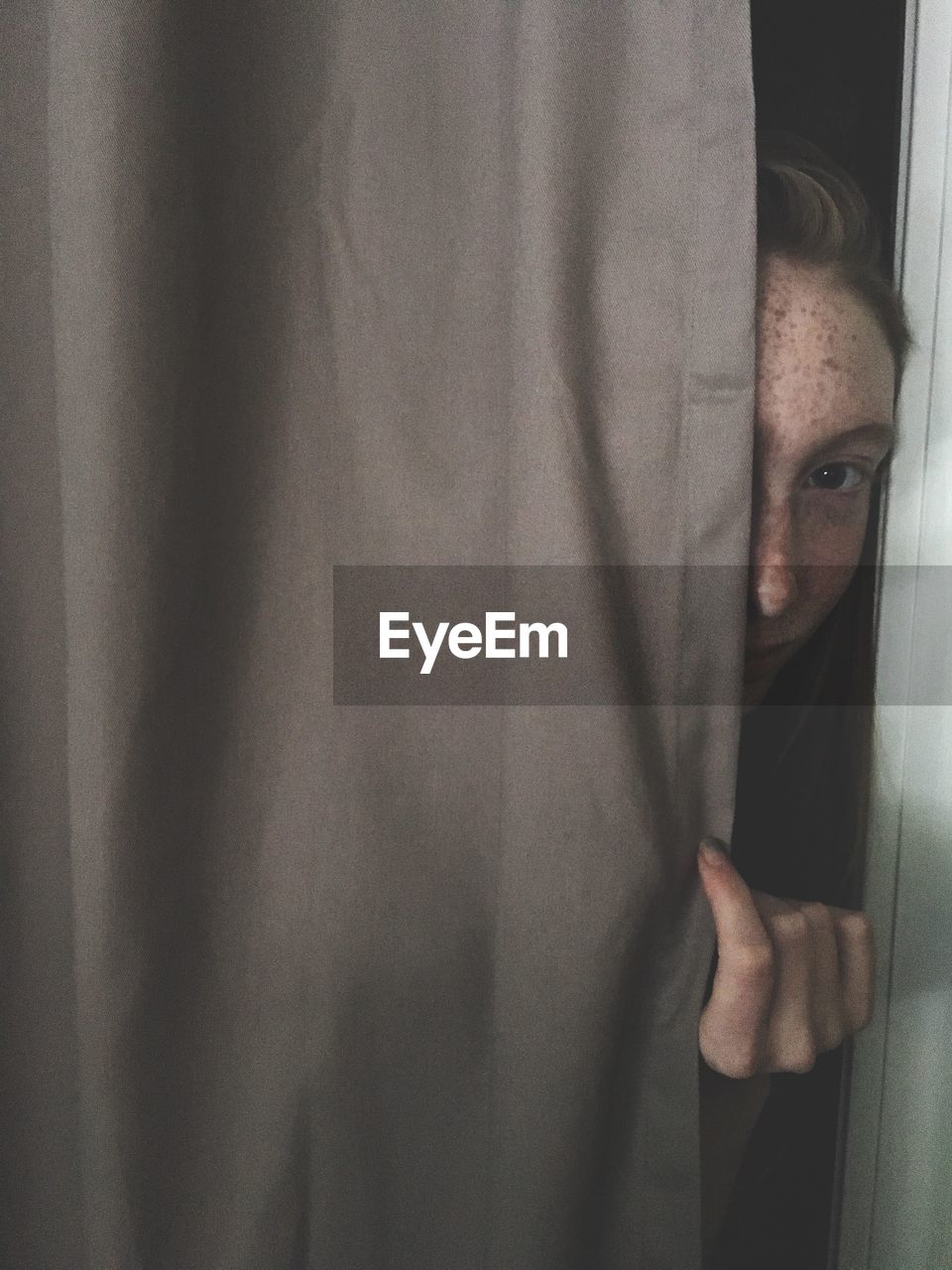 Close-up portrait of teenage girl peeking through curtain at home