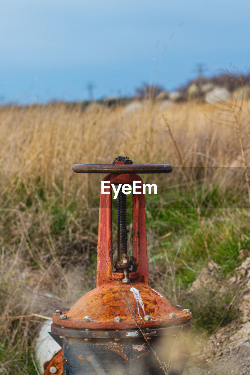 Close-up of rusty metallic structure on field against sky