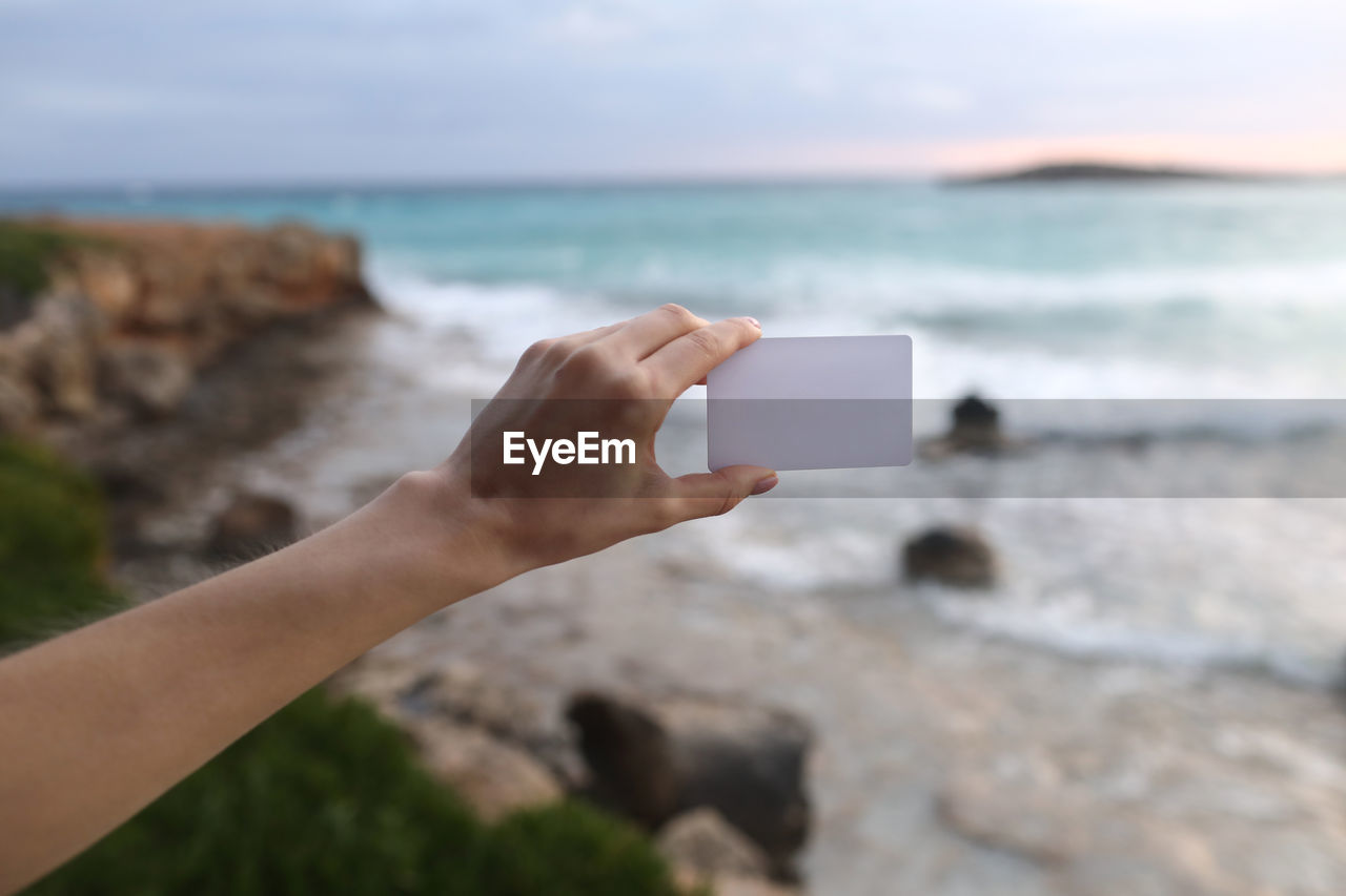 MIDSECTION OF PERSON PHOTOGRAPHING SEA THROUGH CAMERA