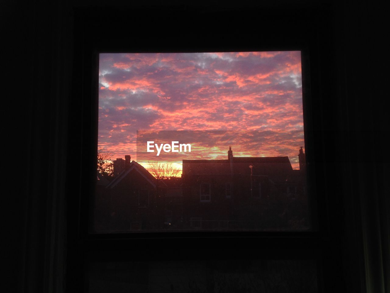 Silhouette buildings against sky during sunset seen through window