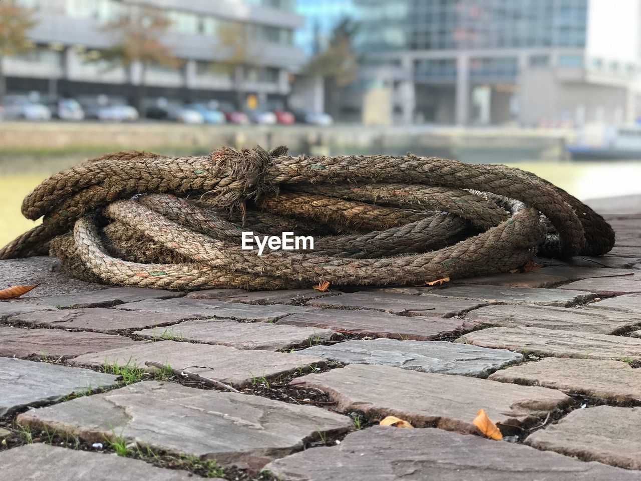 CLOSE-UP OF ROPE TIED ON BOLLARD IN HARBOR