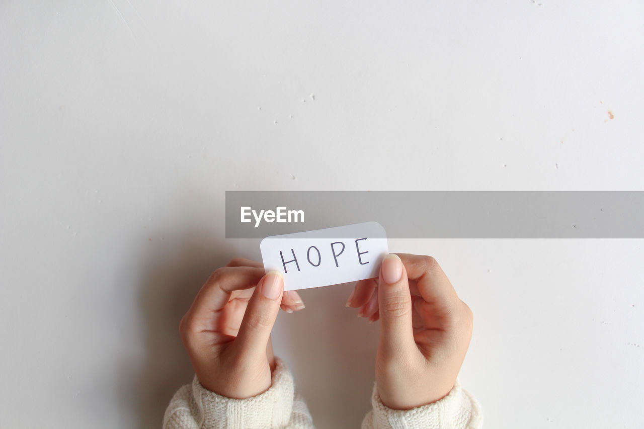 cropped hand of woman holding text on white wall