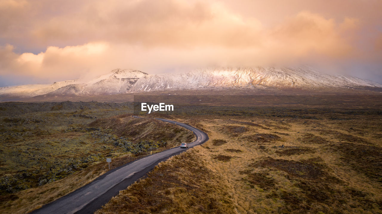 Road by landscape against cloudy sky