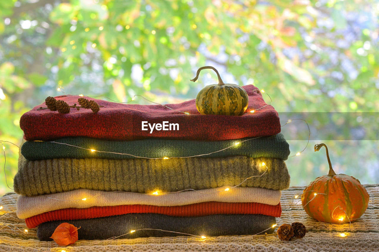 Close-up of illuminated lights on warm clothing and pumpkins and pine cones over table