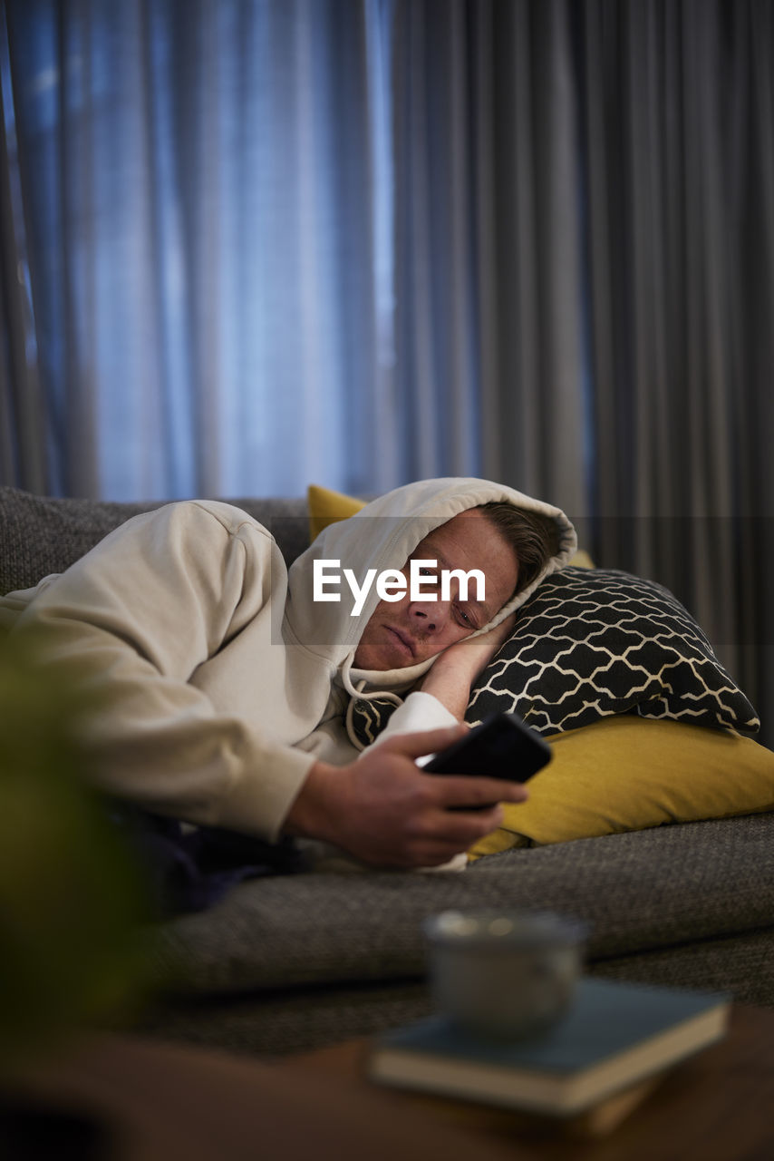 Ill man lying on sofa with smartphone