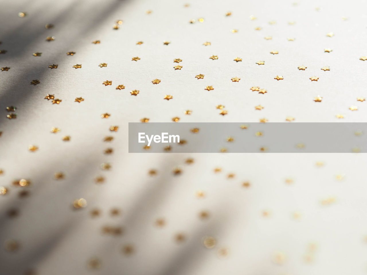 Full frame shot of golden stars confetti on beige background with shadows 